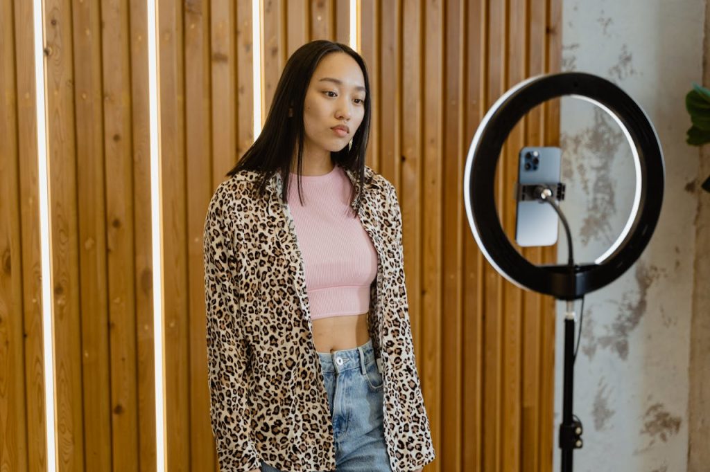 Asian female influencer recording content with ring light and smartphone indoors.