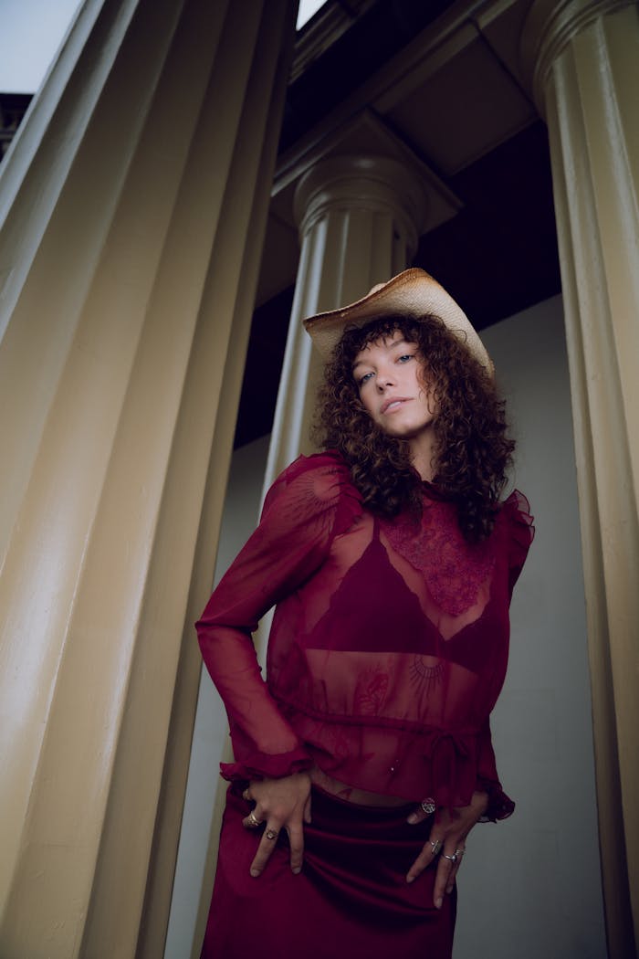 Stylish woman in red outfit poses confidently by columns, wearing a cowboy hat.