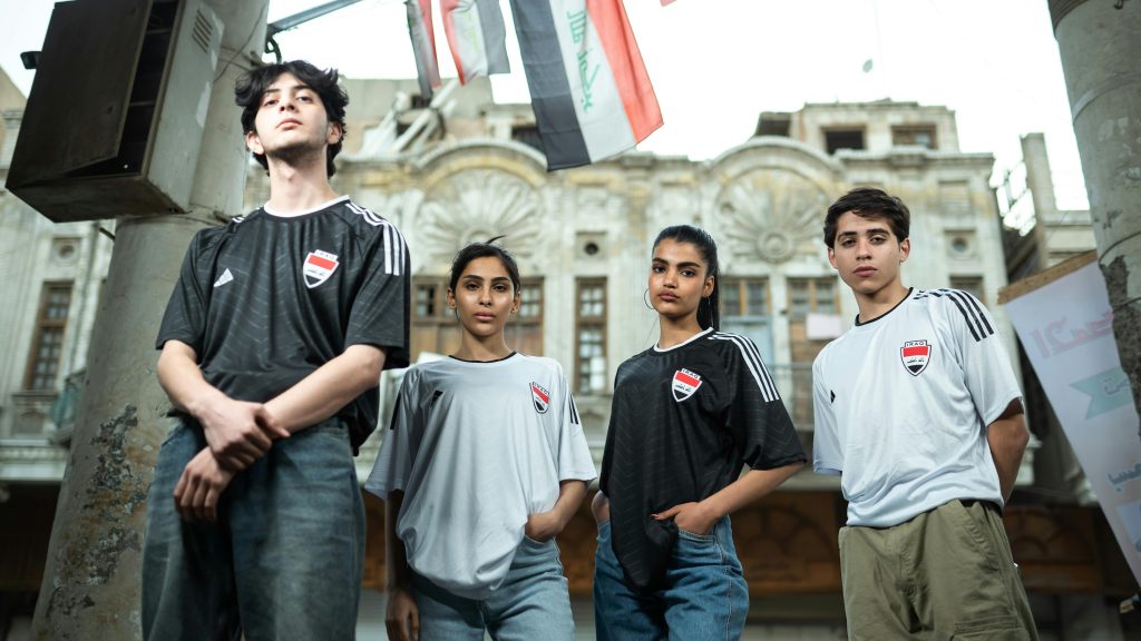Four young adults in soccer jerseys posing in an urban outdoor setting.