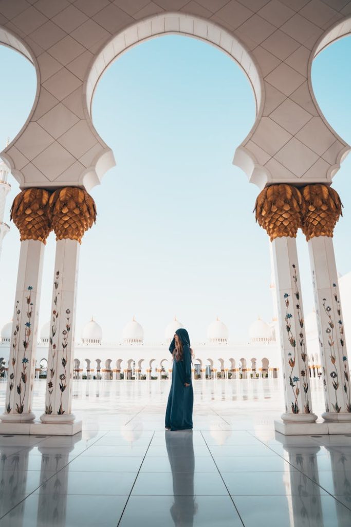 A person in traditional attire standing among columns of the Sheikh Zayed Mosque in Abu Dhabi.