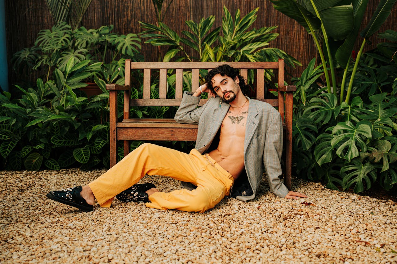 Stylish model relaxing on bench, showcasing contemporary fashion amidst lush greenery.